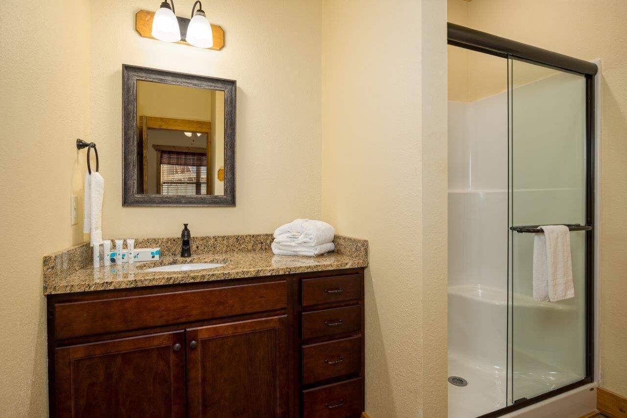 A bathroom with a granite countertop, a dark wooden vanity, a mirror, and a glass-enclosed shower.