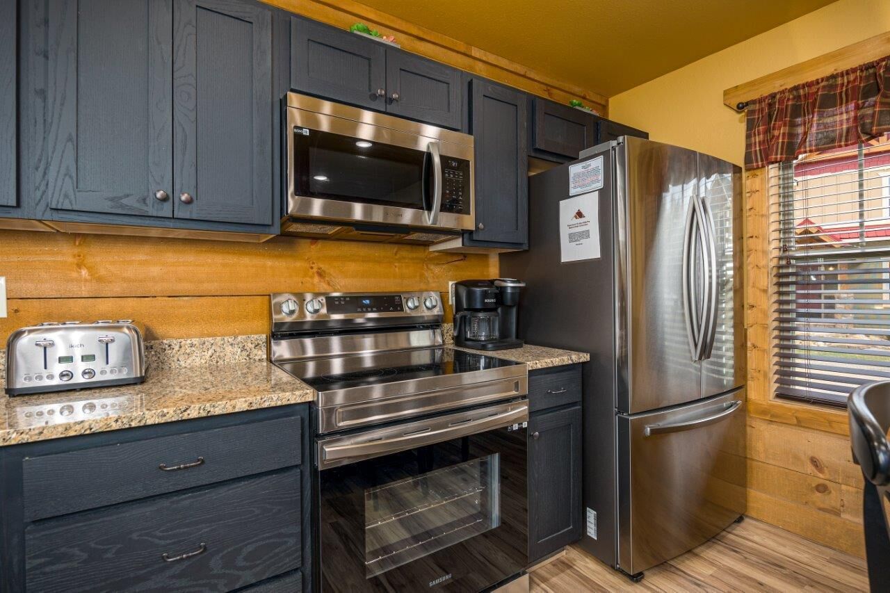 A modern kitchen with dark cabinets, stainless steel appliances including a microwave, oven, and refrigerator, and a toaster on the counter.