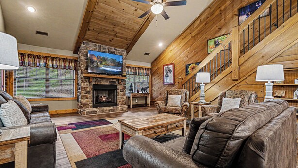 A wooden interior with a stone fireplace, leather sofas, a television, and a staircase. - Ivie Holler (Gatlinburg)