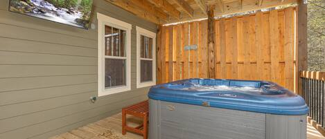 A wooden deck with a hot tub, a wooden chair, and a television mounted on the wall.