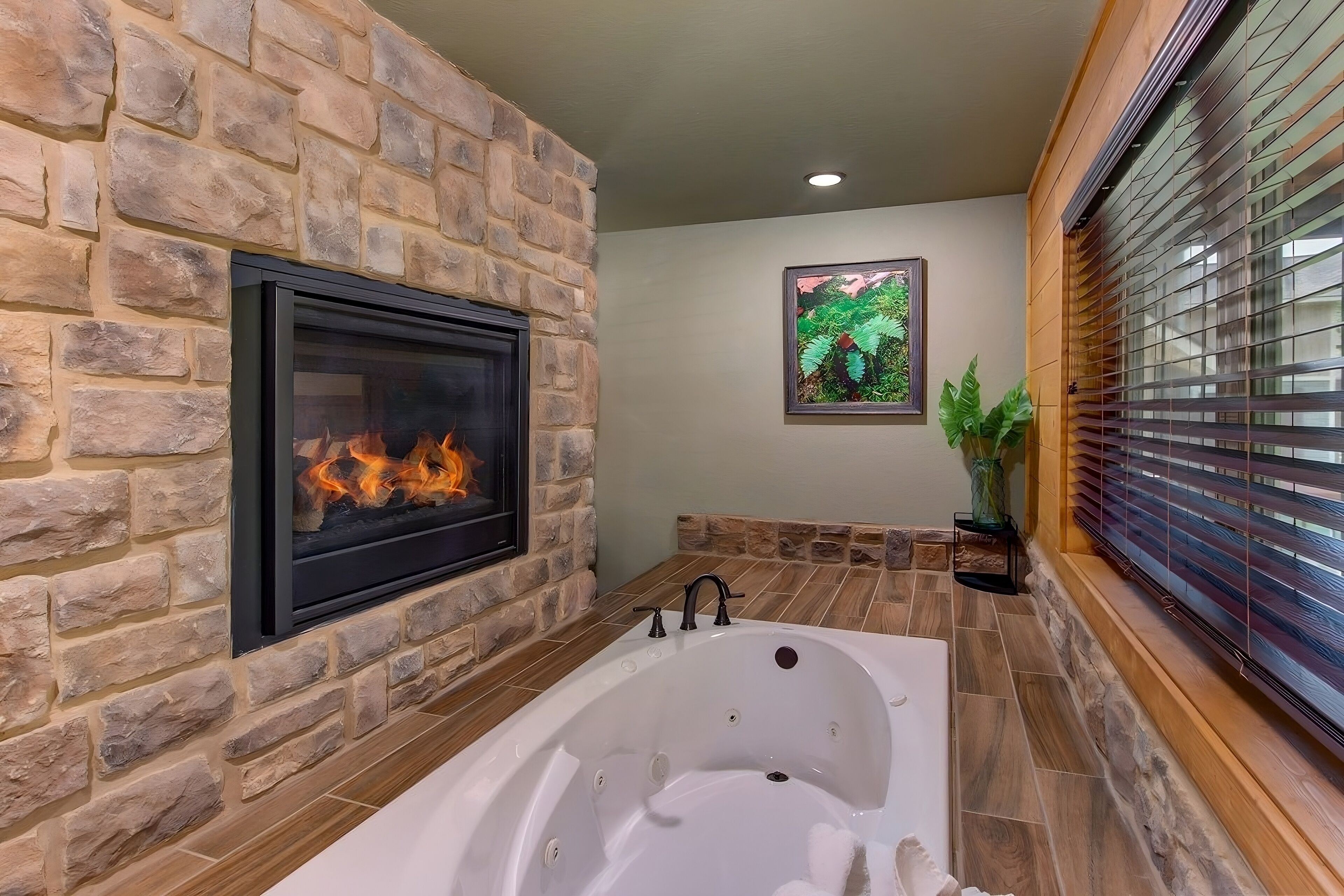 A bathroom with a stone wall, a fireplace, a bathtub, and a window with blinds.