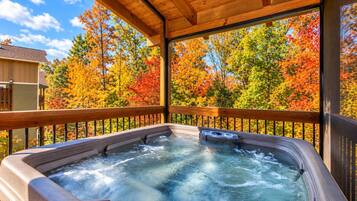 A hot tub with a wooden deck and a view of autumn trees.