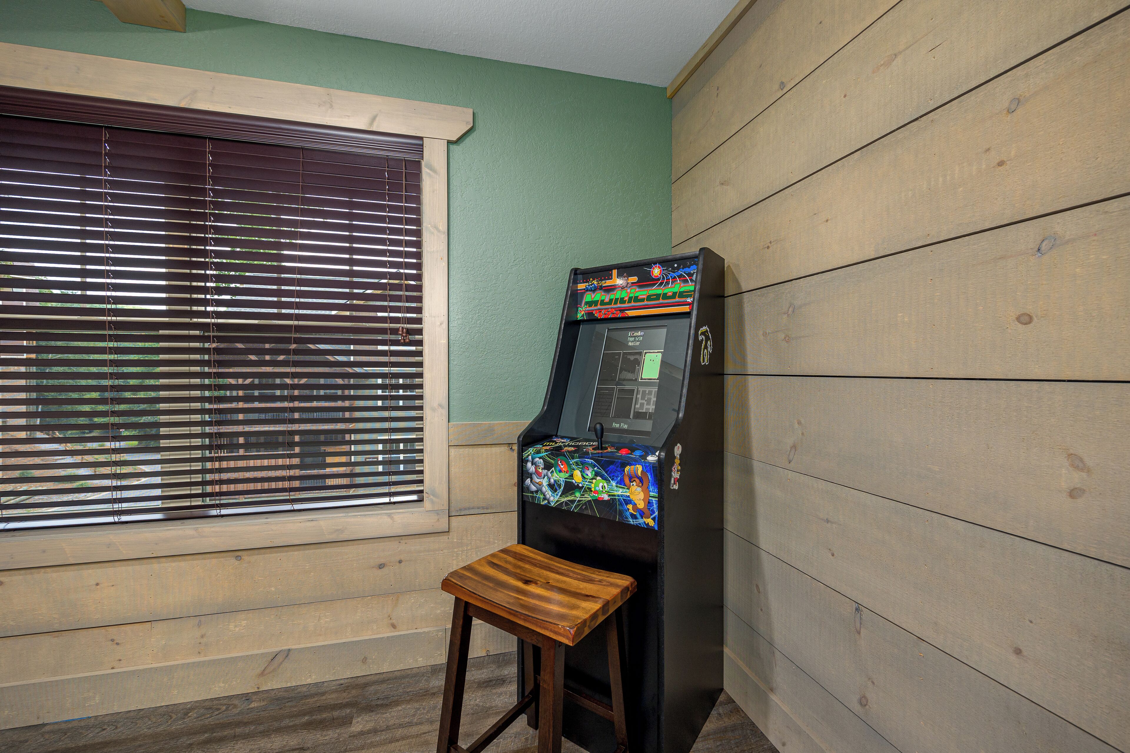 A room with a wooden floor, a window with blinds, and a single arcade game machine.