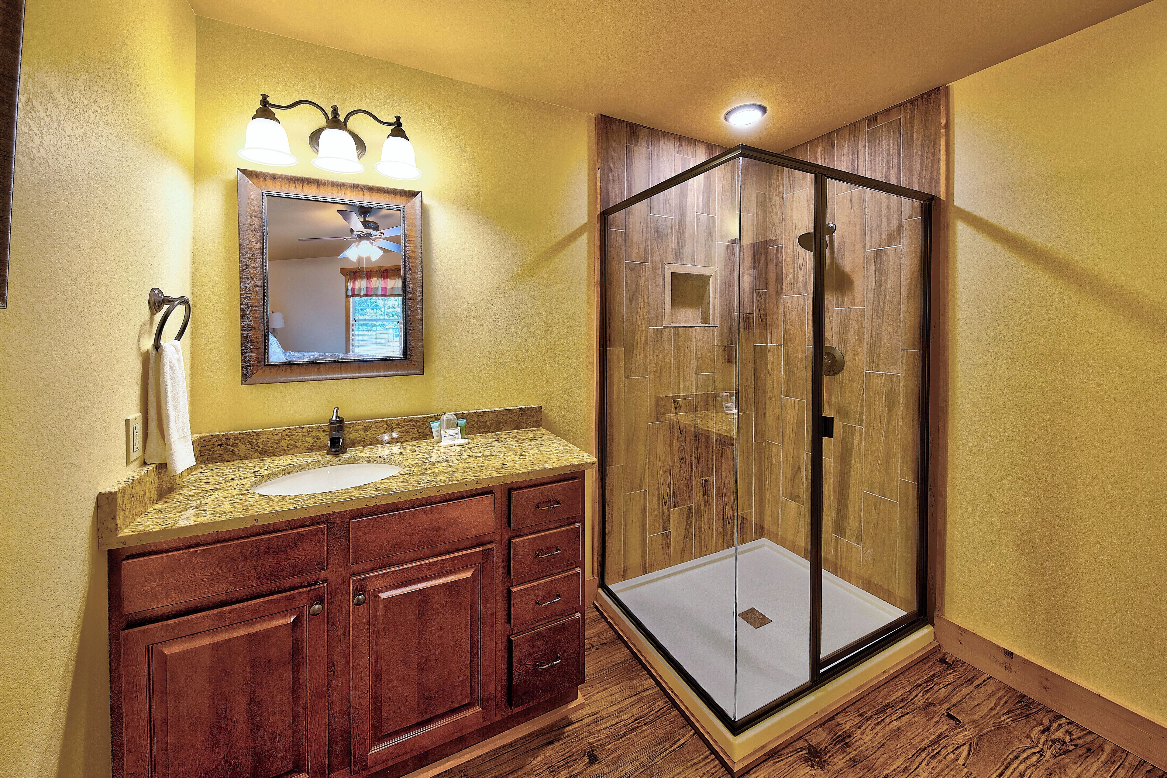 Une salle de bain avec un meuble-lavabo en bois, une cabine de douche en verre et un miroir avec des lumières au-dessus du lavabo.