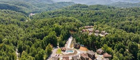 Un complejo turístico con varias edificaciones, una piscina y un paisaje boscoso circundante.