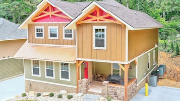 A two-story house with a front porch, stone foundation, and a red door.