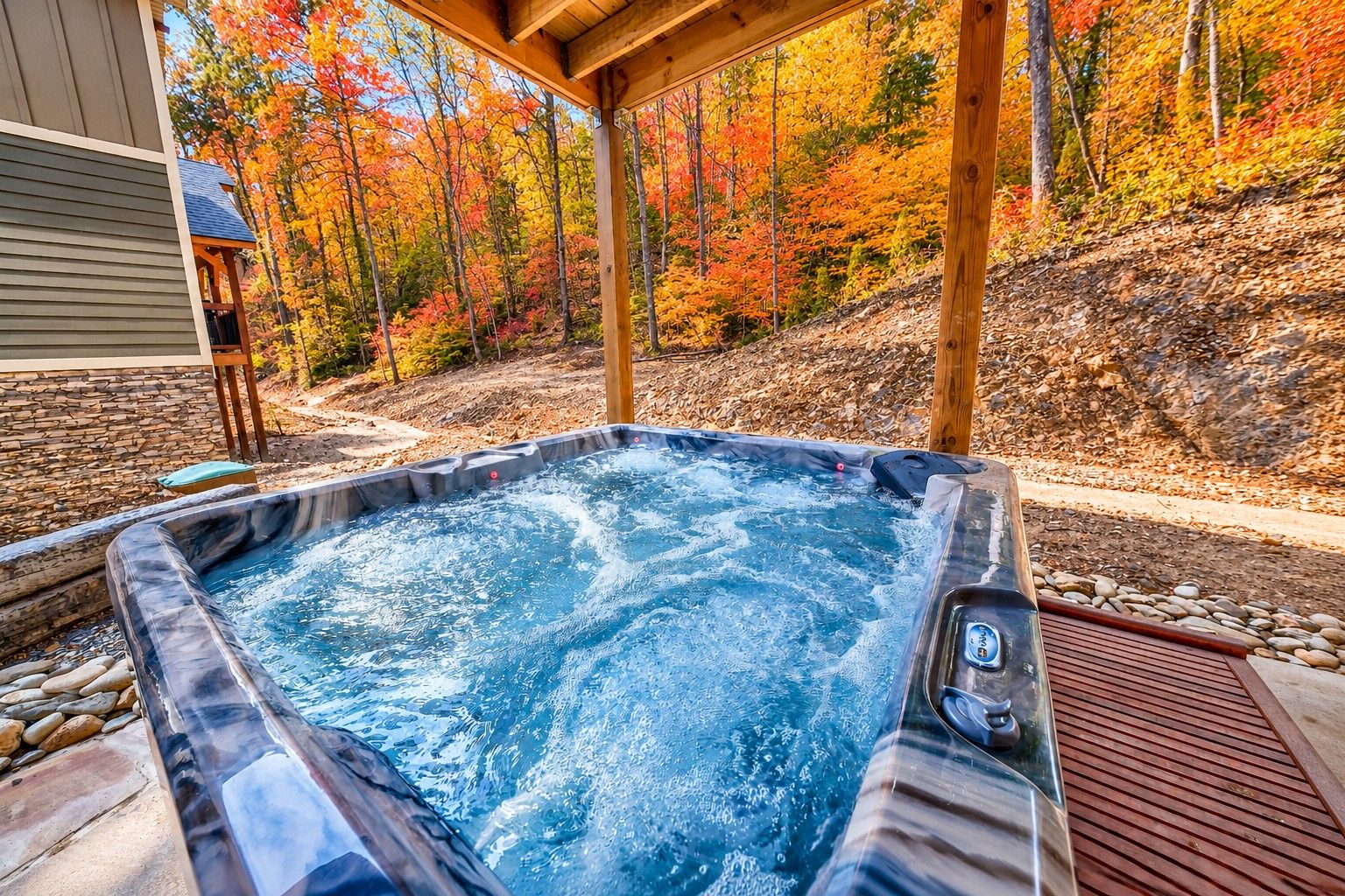 A hot tub with a wooden deck and a stone wall in the background.