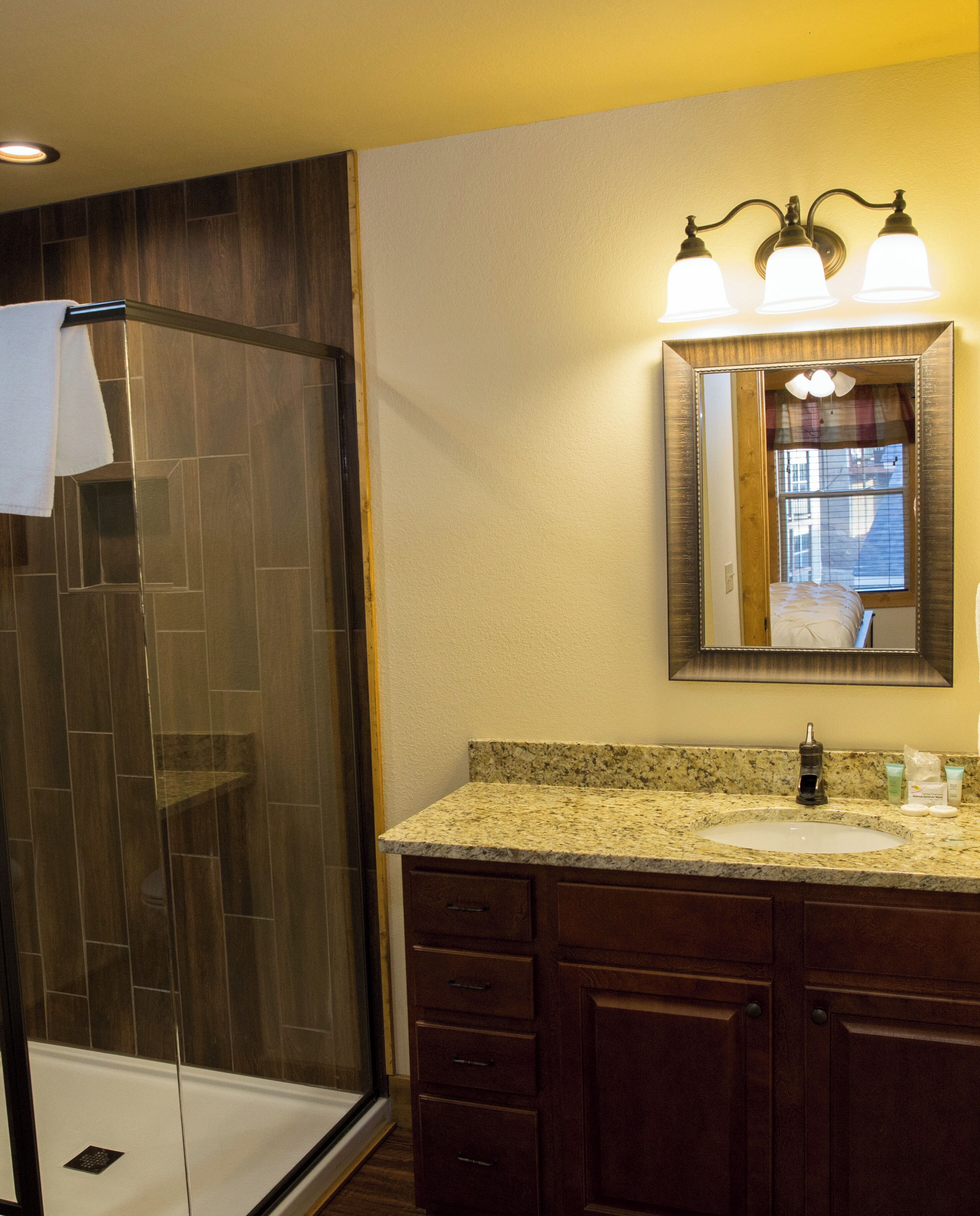 A bathroom with a shower, a sink with a vanity, and a mirror with lights.
