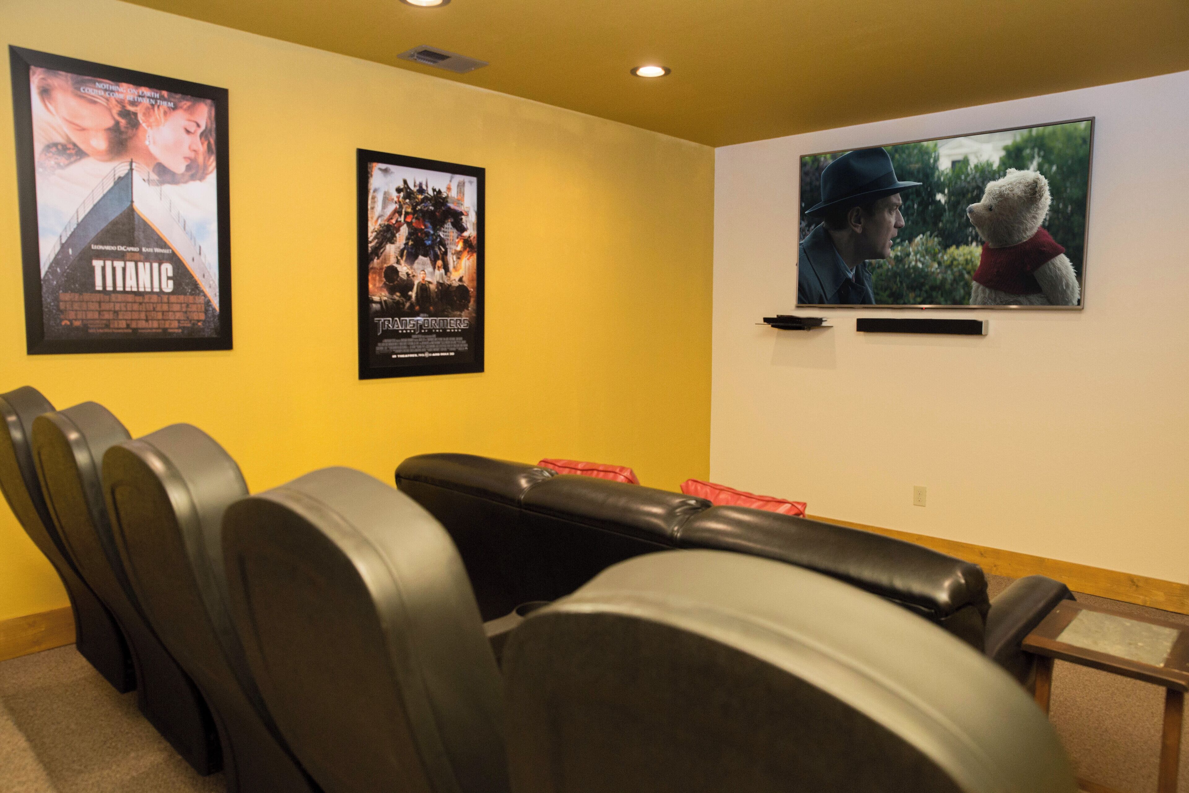 A cinema room with black leather seats, two movie posters on the wall, and a television screen.