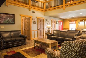 A spacious living room with two leather sofas, a wooden coffee table, and a patterned armchair. A wooden door and a wall-mounted lamp are also visible. - Gatlinburg Pool Pad (Gatlinburg)