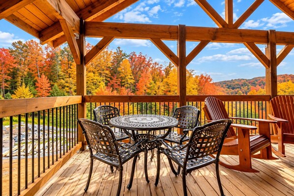 A wooden deck with a table and chairs, surrounded by a railing, overlooking a forest with autumn foliage. - Almost Heaven (Gatlinburg)