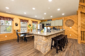 A kitchen with a stone island, wooden cabinets, and a bar area. - Pirates Peak (Gatlinburg)