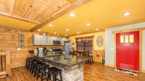 A kitchen with a central island, bar stools, wooden flooring, and a red door. - Moonshine Manor (Gatlinburg)