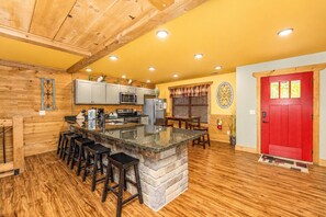 A kitchen with a central island, bar stools, wooden flooring, and a red door. - Moonshine Manor (Gatlinburg)