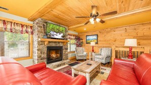 A cozy living room with a stone fireplace, red leather sofas, a television, and a ceiling fan. - Moonshine Manor (Gatlinburg)