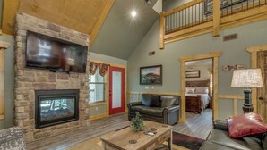 A spacious living room with a stone fireplace, a flat-screen TV, a wooden coffee table, and a leather sofa. - Marco Polo (Gatlinburg)