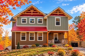 A two-story house with a red roof, stone foundation, and a front porch with a bench. - Firefly Nights (Gatlinburg)