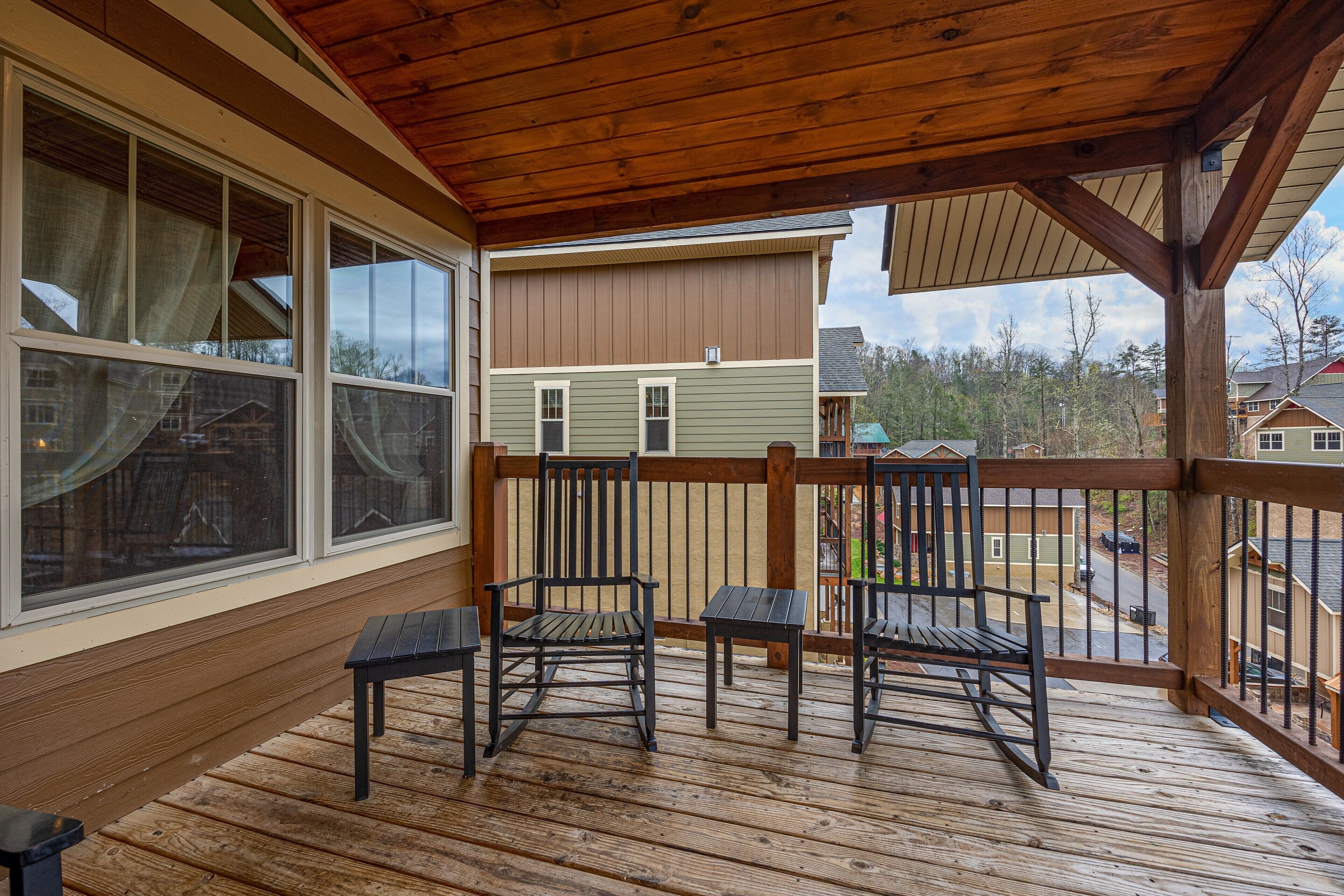 A wooden deck with two rocking chairs and a table, overlooking a residential area.