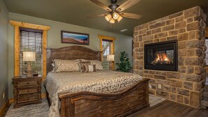 A bedroom with a large bed, a stone fireplace, and a ceiling fan. - Serenity Peak (Gatlinburg)