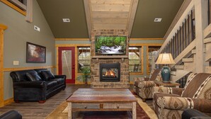A spacious living room with a stone fireplace, comfortable seating, and a television. - Serenity Peak (Gatlinburg)