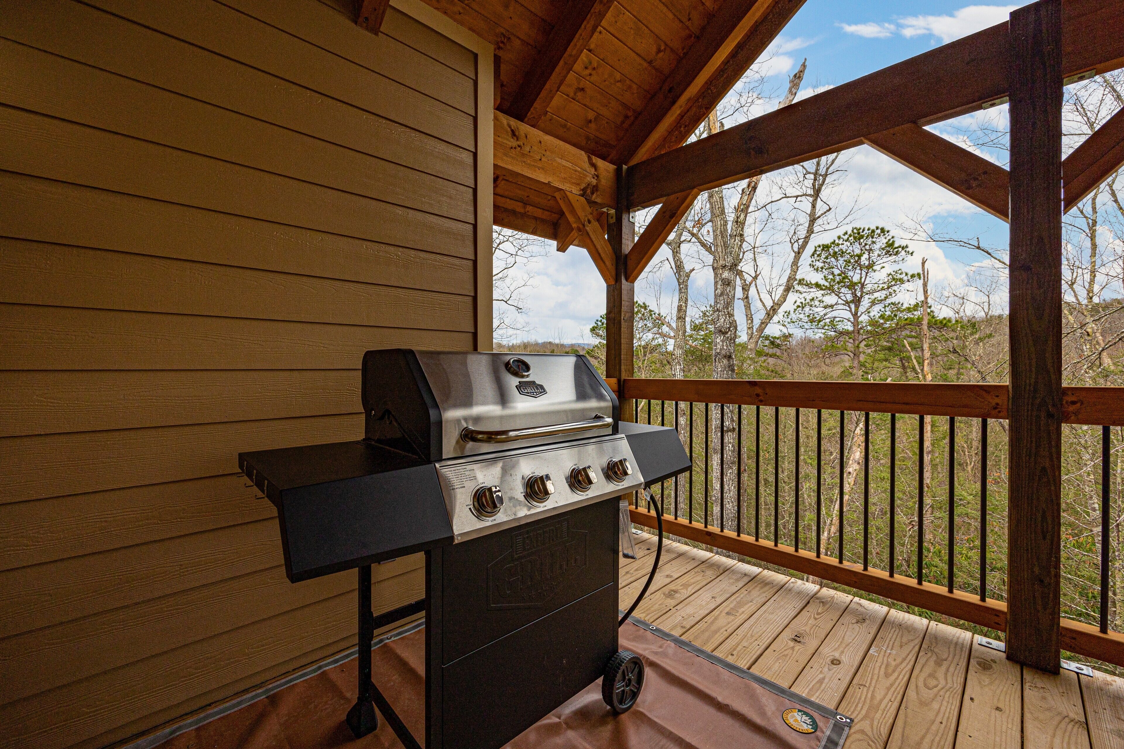 A barbecue grill on a wooden deck with a view of trees and sky.