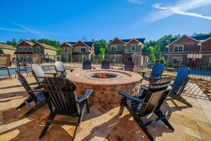 Een terras met een ronde vuurkuil, omringd door Adirondack-stoelen, een zwembad en een rij huizen op de achtergrond.