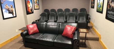 A home theater room with a black leather couch, red cushions, and a row of black theater seats.