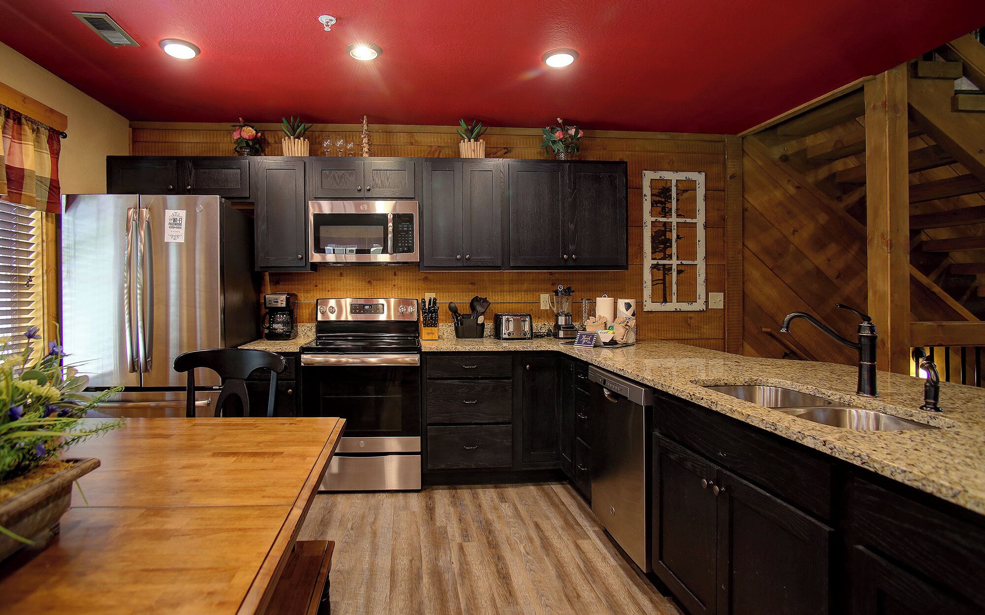 Cocina pequeña con armarios oscuros, electrodomésticos de acero inoxidable y piso de madera.