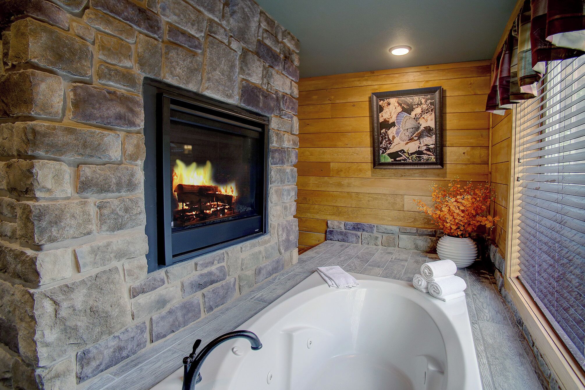 A stone fireplace with a fire, a framed picture on the wall, and a white bathtub with towels.