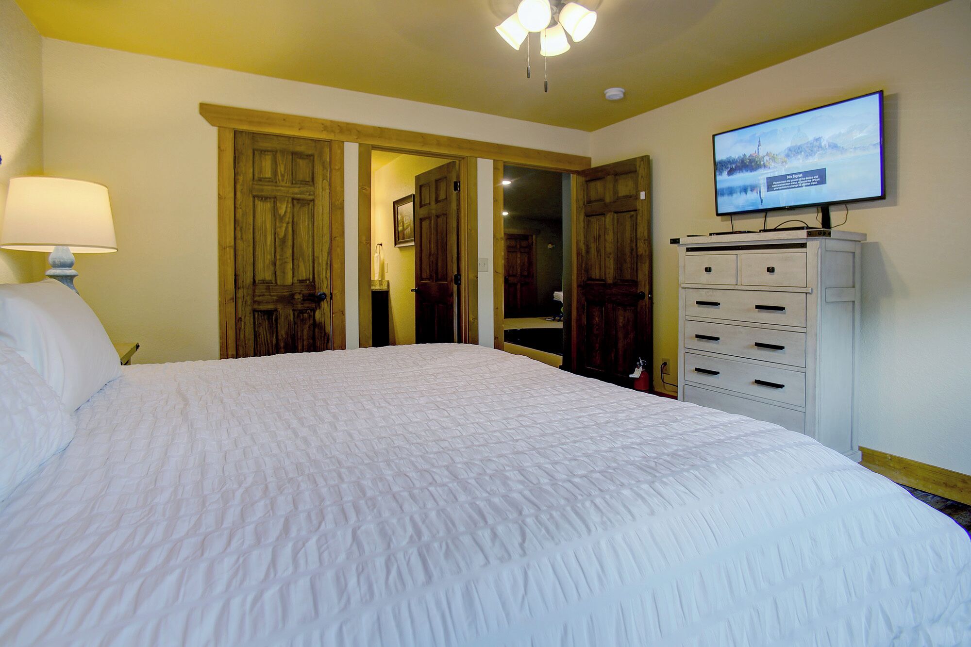 A hotel room with a large bed, wooden doors, a dresser, and a television on the wall.