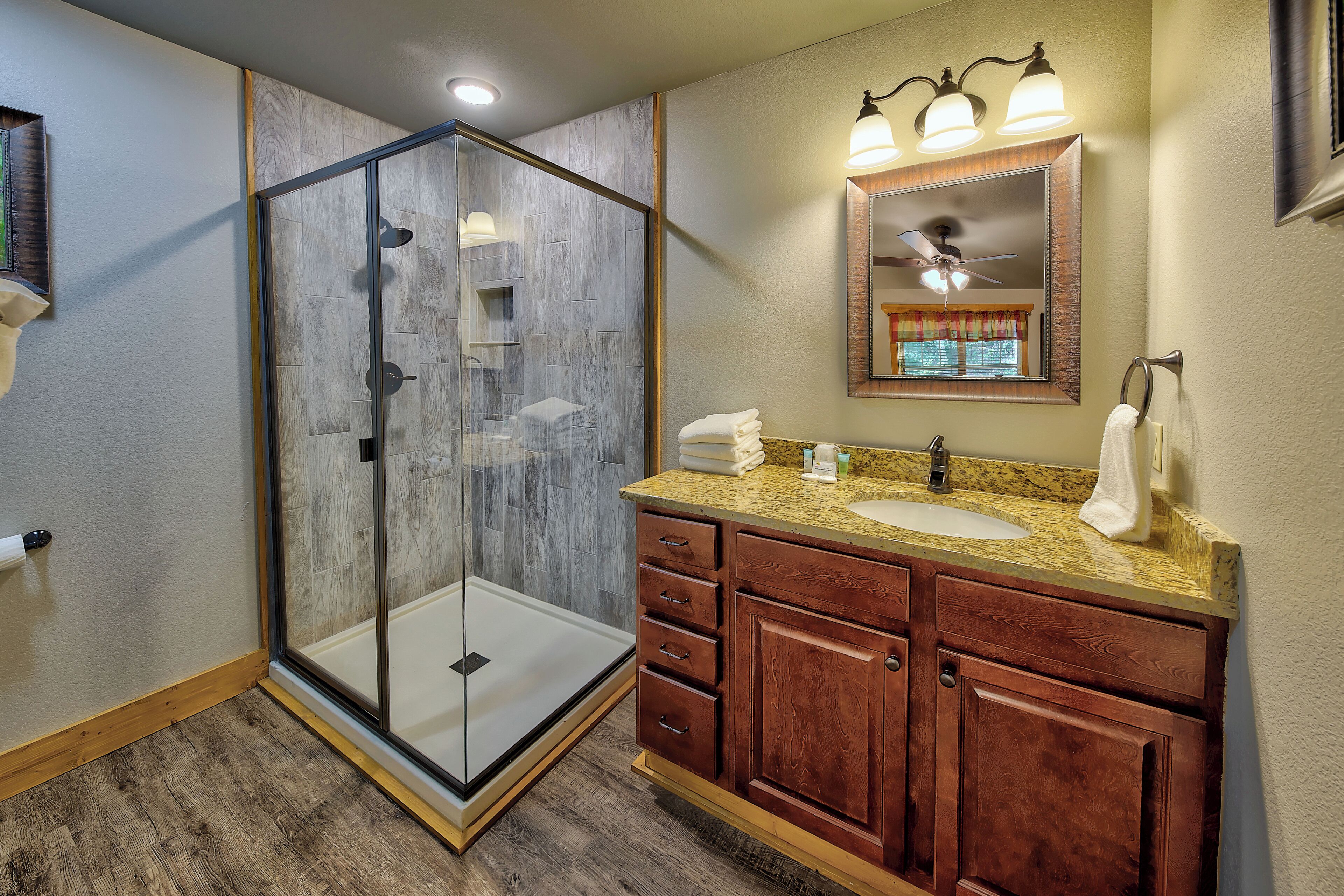 A bathroom with a glass-enclosed shower, a sink with a vanity, and a ceiling fan.