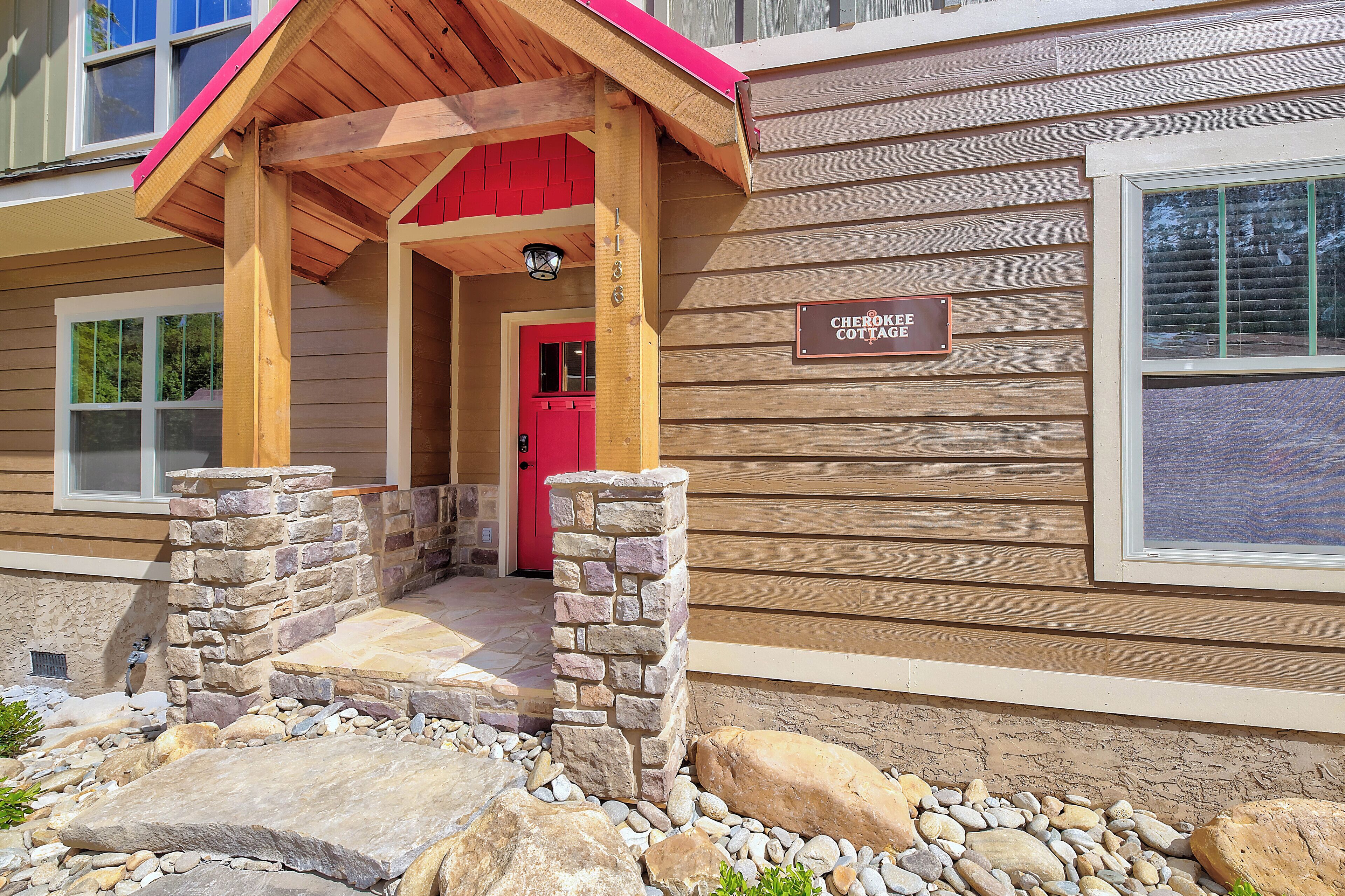 A wooden cottage with a stone pillar entrance, a red door, and a sign reading "Cherokee Cottage."