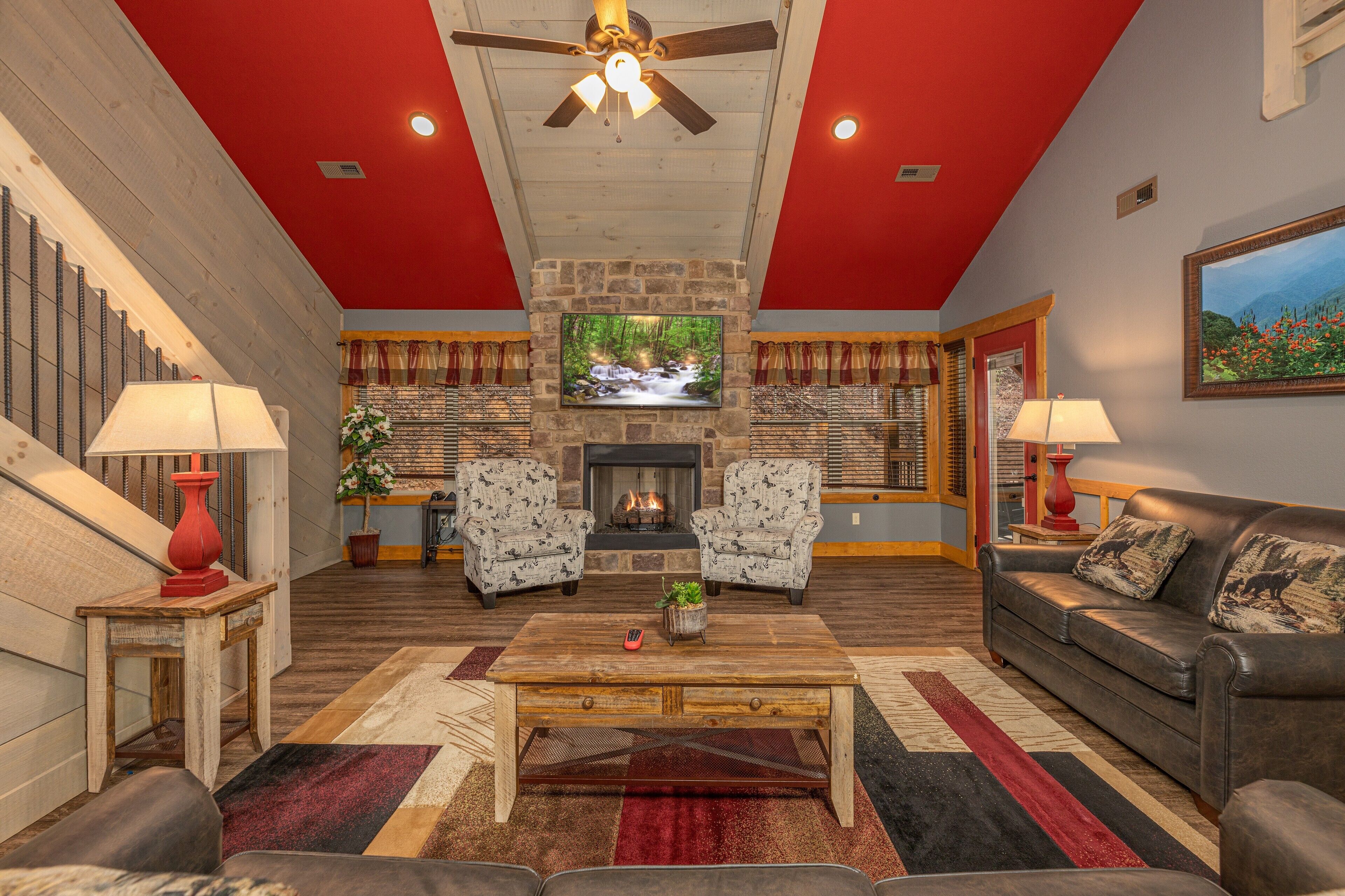 Un salon spacieux avec une cheminée, deux fauteuils à motifs, un canapé, une table basse et un escalier dont le plafond est peint en rouge.