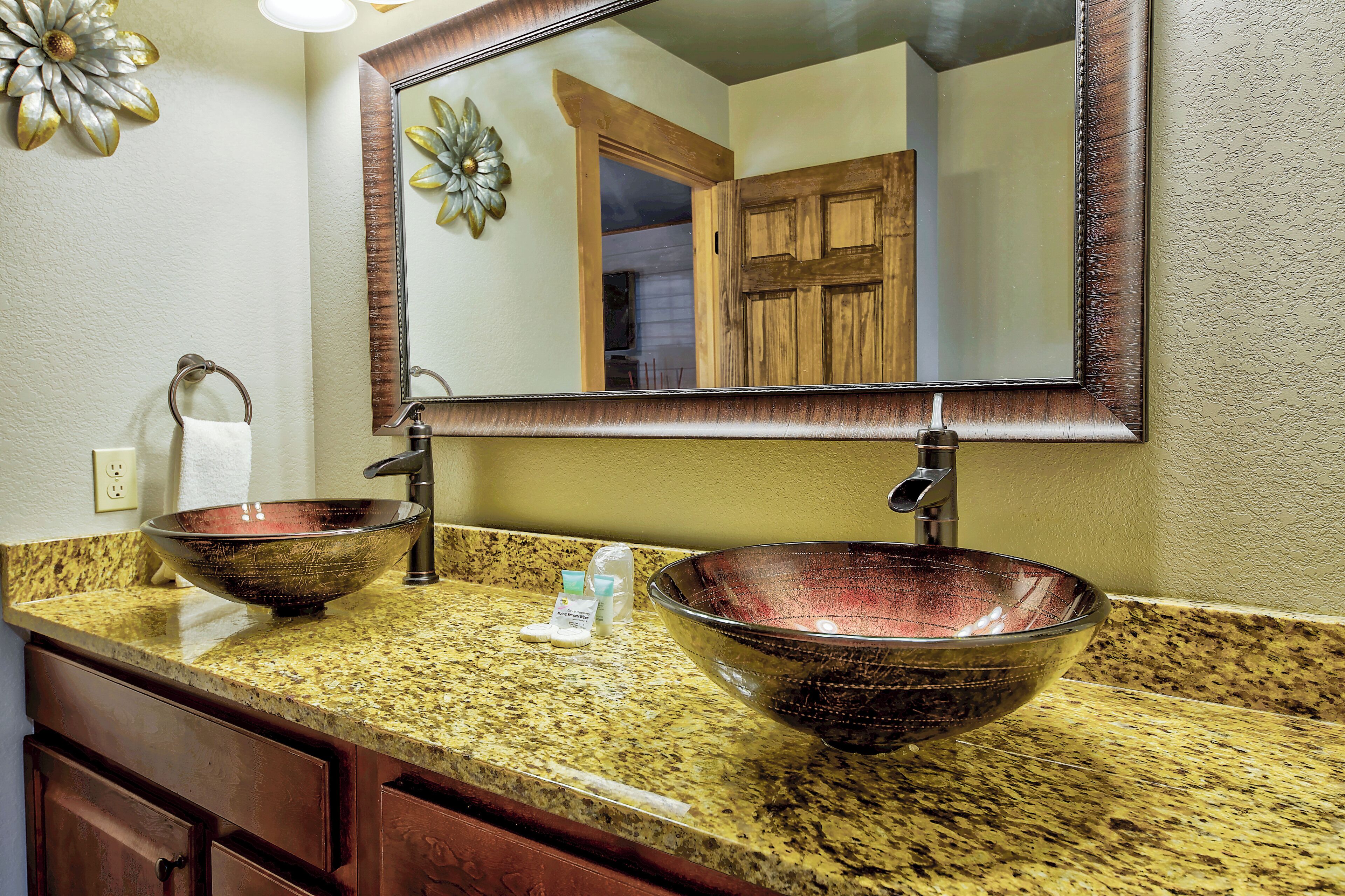 A bathroom with a granite countertop, two vessel sinks, a mirror, and wooden cabinets.