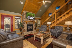 A cozy living room with a stone fireplace, wooden ceiling, and a staircase. - Fireside Retreat (Gatlinburg)
