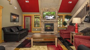 A living room with a stone fireplace, red walls, a black leather sofa, and a red armchair. - Southern Comfort (Gatlinburg)