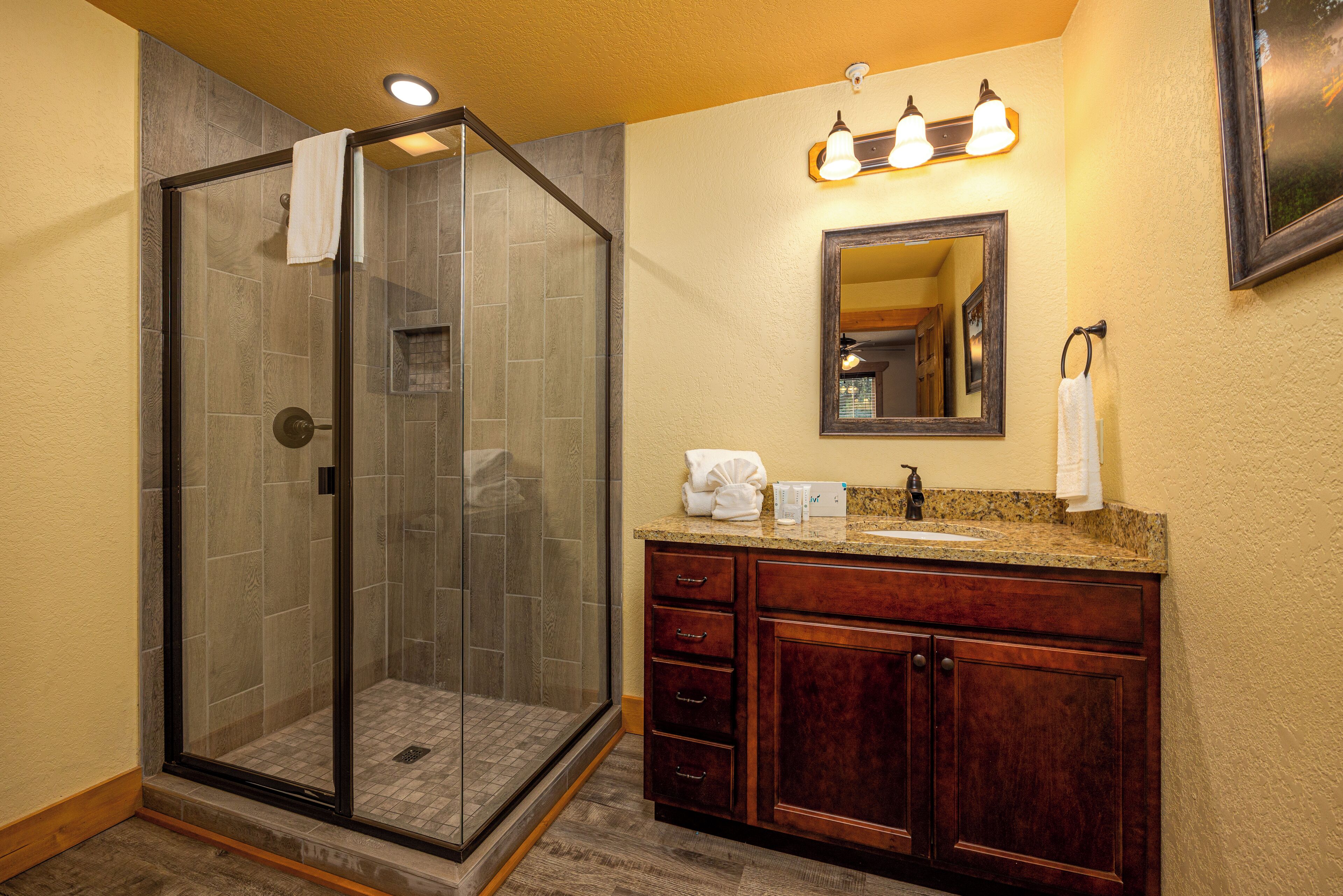 A bathroom with a glass-enclosed shower, a vanity with a granite countertop, and a mirror above the sink.