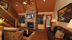 A cozy living room with a stone fireplace, wooden ceiling, and a staircase leading to another level. - Misty Mountainside (Gatlinburg)