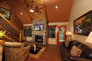 A cozy living room with a stone fireplace, wooden ceiling, and a staircase. - Misty Mountainside (Gatlinburg)