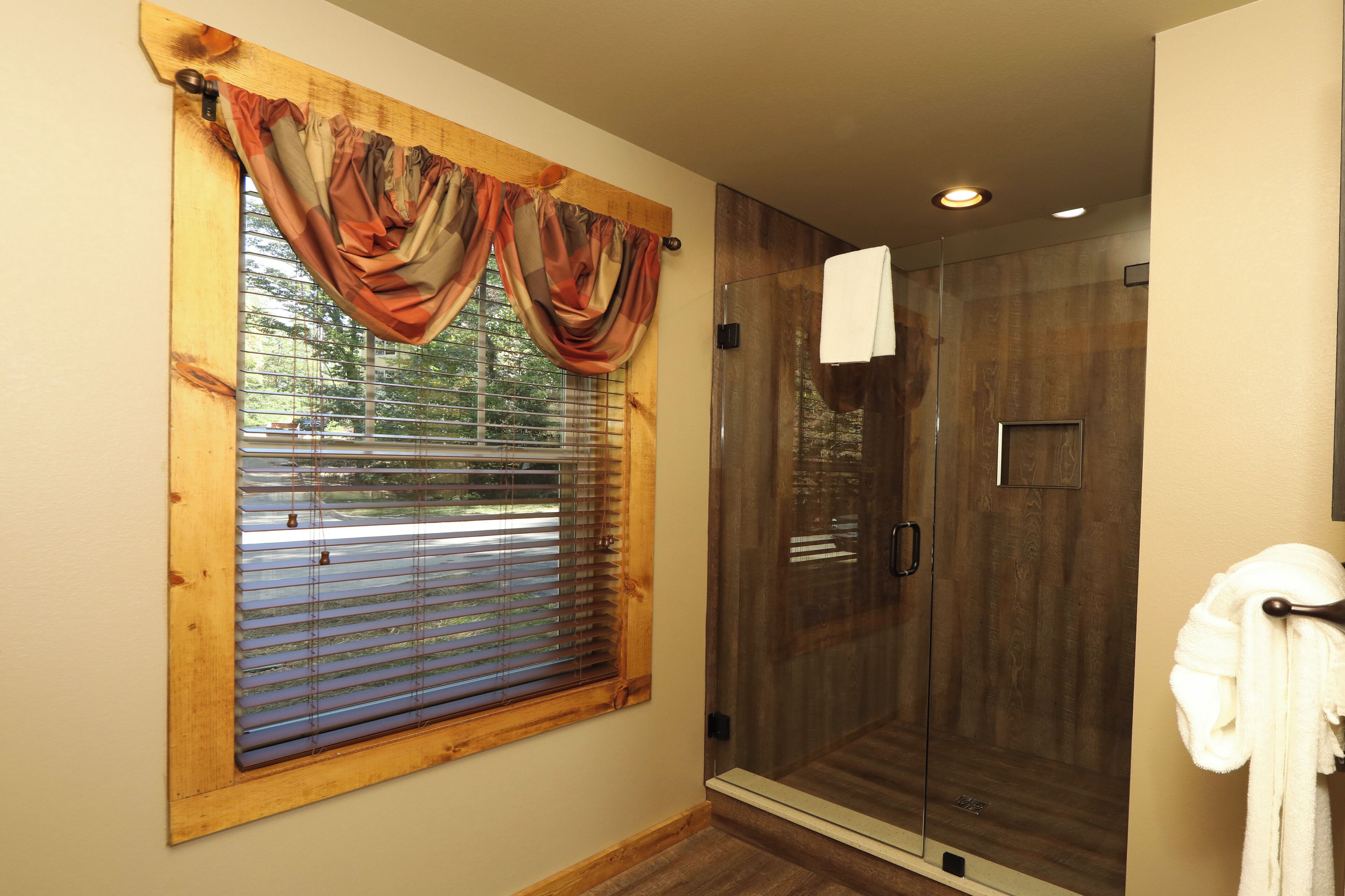 Une salle de bain avec une fenêtre à cadre en bois, une douche en verre et une serviette accrochée au mur.