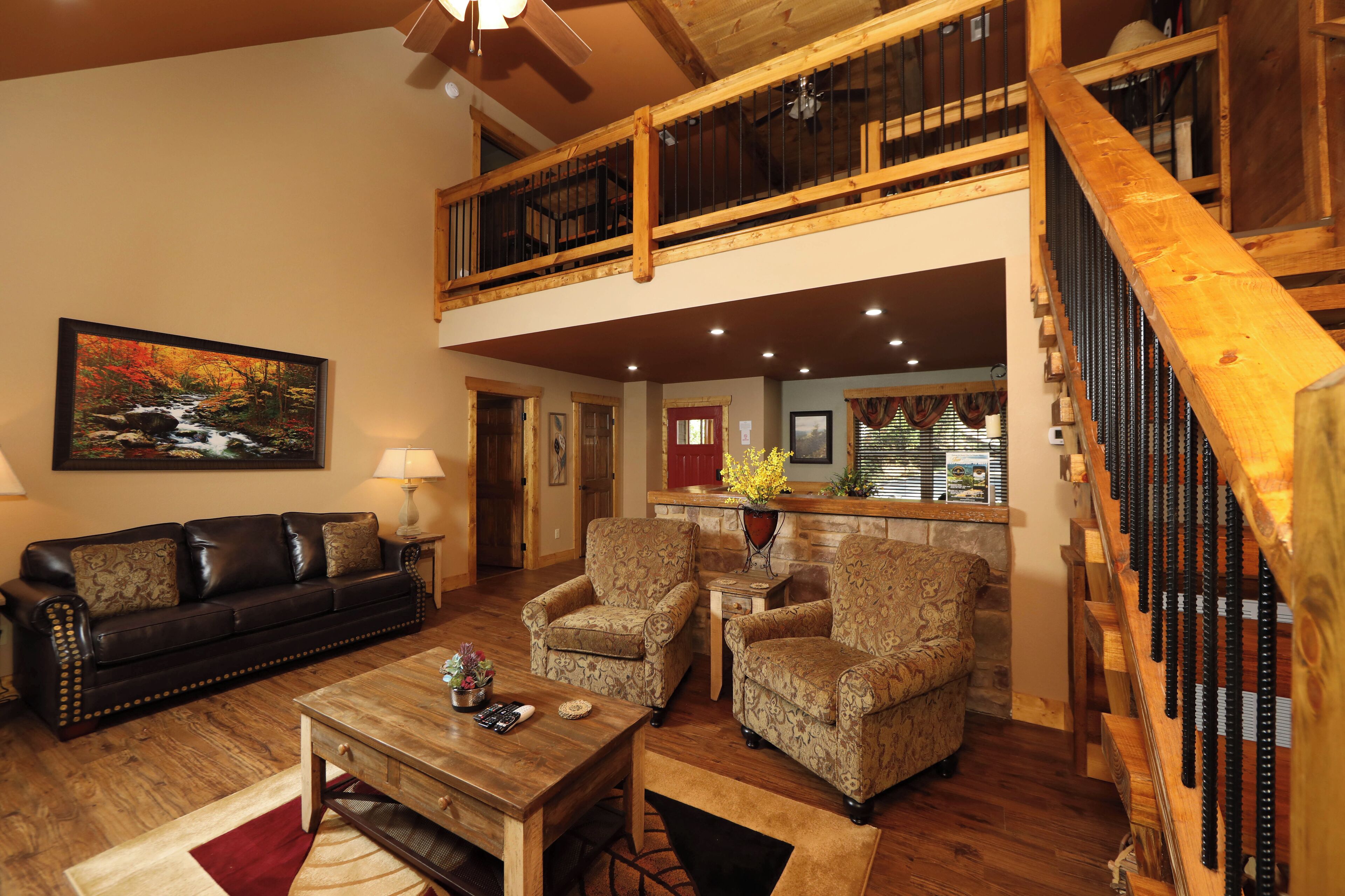 A spacious living room with a high ceiling, a wooden staircase, and a dining area with a kitchen in the background.