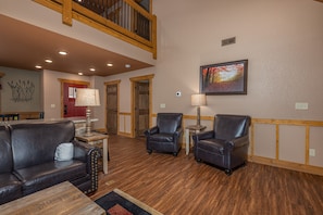 A spacious living area with a high ceiling, wooden beams, and a fireplace. There are two leather armchairs and a sofa. - Heavenly Haven (Gatlinburg)