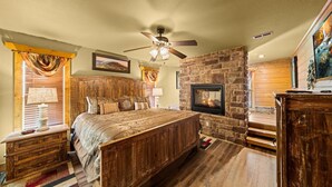 A bedroom with a wooden bed, a stone fireplace, a ceiling fan, and a painting on the wall. - Splash Mansion (Gatlinburg)