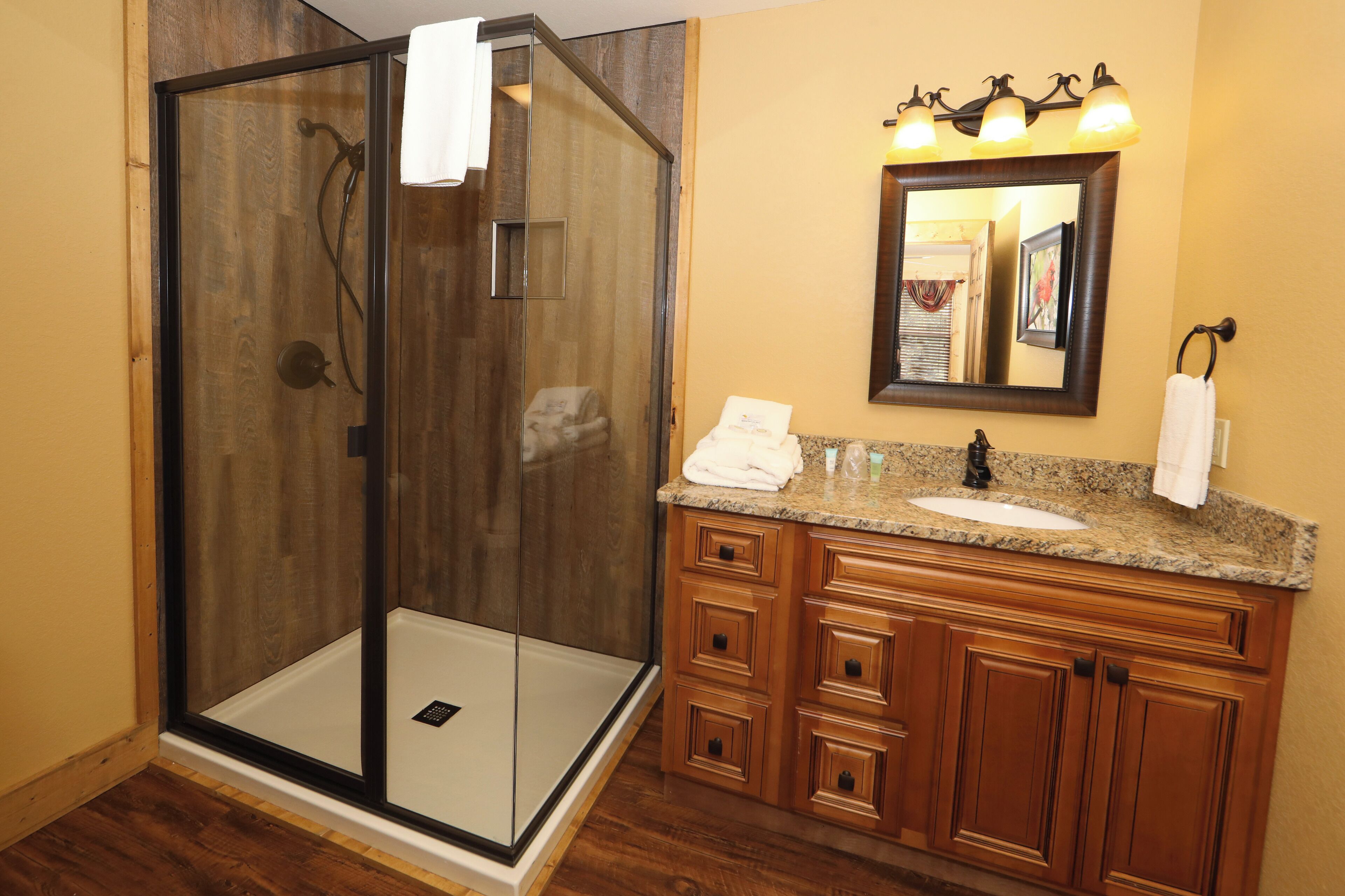 Une salle de bain dotée d’une douche à parois de verre, d’un meuble-lavabo en bois et d’un miroir au-dessus du meuble.