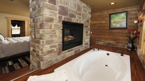 Ein Badezimmer mit Kamin aus Stein, einer großen Badewanne und Holzwänden.
