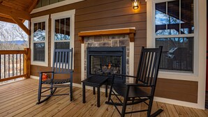 Une terrasse en bois avec une cheminée en pierre, deux fauteuils à bascule et une table.