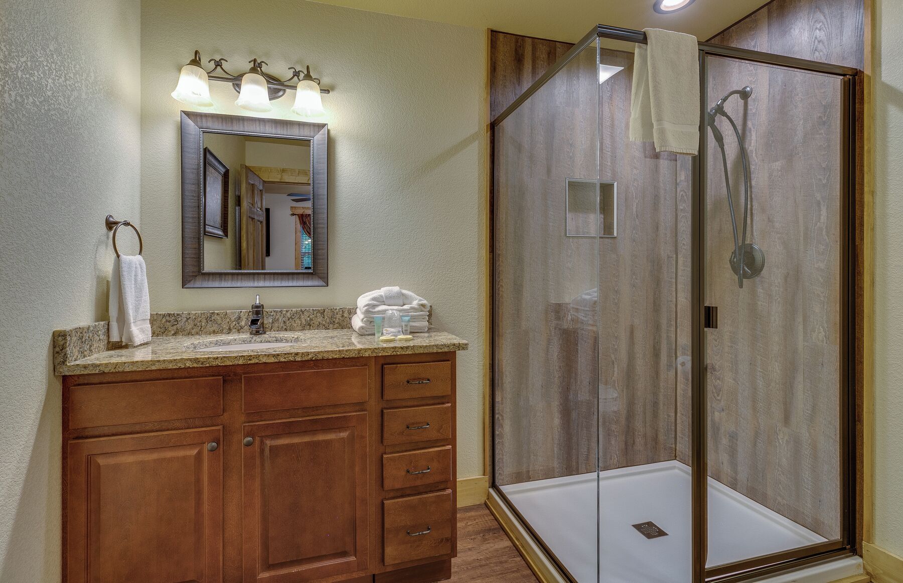 Une salle de bain avec un meuble-lavabo en bois, un miroir, une cabine de douche en verre et un porte-serviettes.