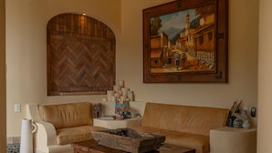 Een woonkamer met een kamerdeuren in visgraatmotief, een schilderij van een dorpsgezicht, een beige bank, een houten bijzettafeltje en een decoratieve vaas.