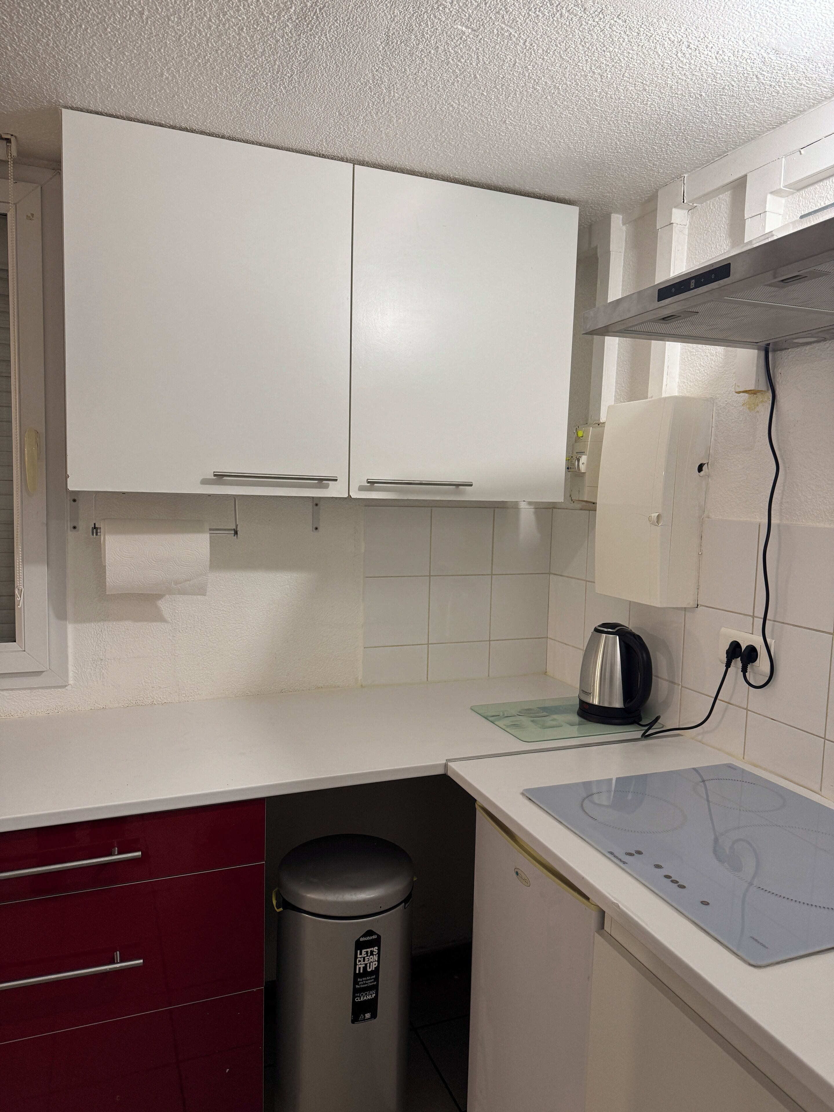 A kitchen with white cabinets, a stainless steel kettle, and a trash bin.