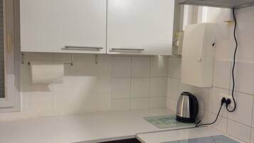 A kitchen with white cabinets, a stainless steel kettle, and a trash bin.